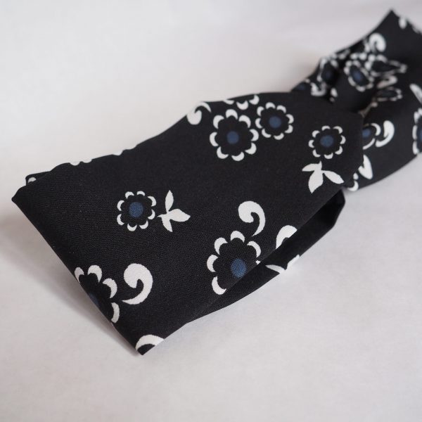 Bandeau pour cheveux croisé en polyester noir à fleurs blanches.